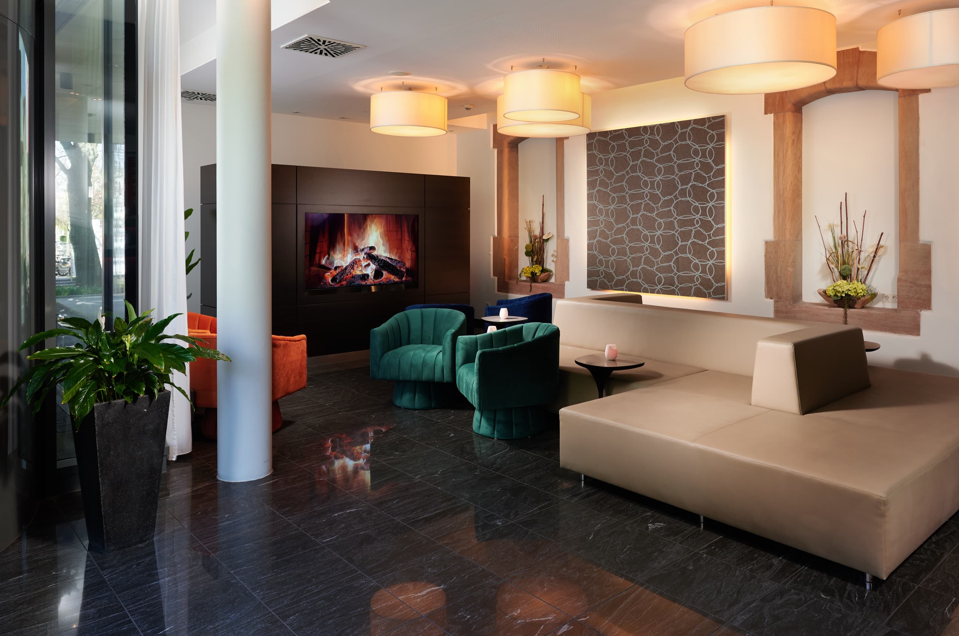 Elegante Lounge im NOVINA Hotel Tillypark Nürnberg mit türkisfarbenen Sesseln, Kamin und Säulen in warmem Abendlicht