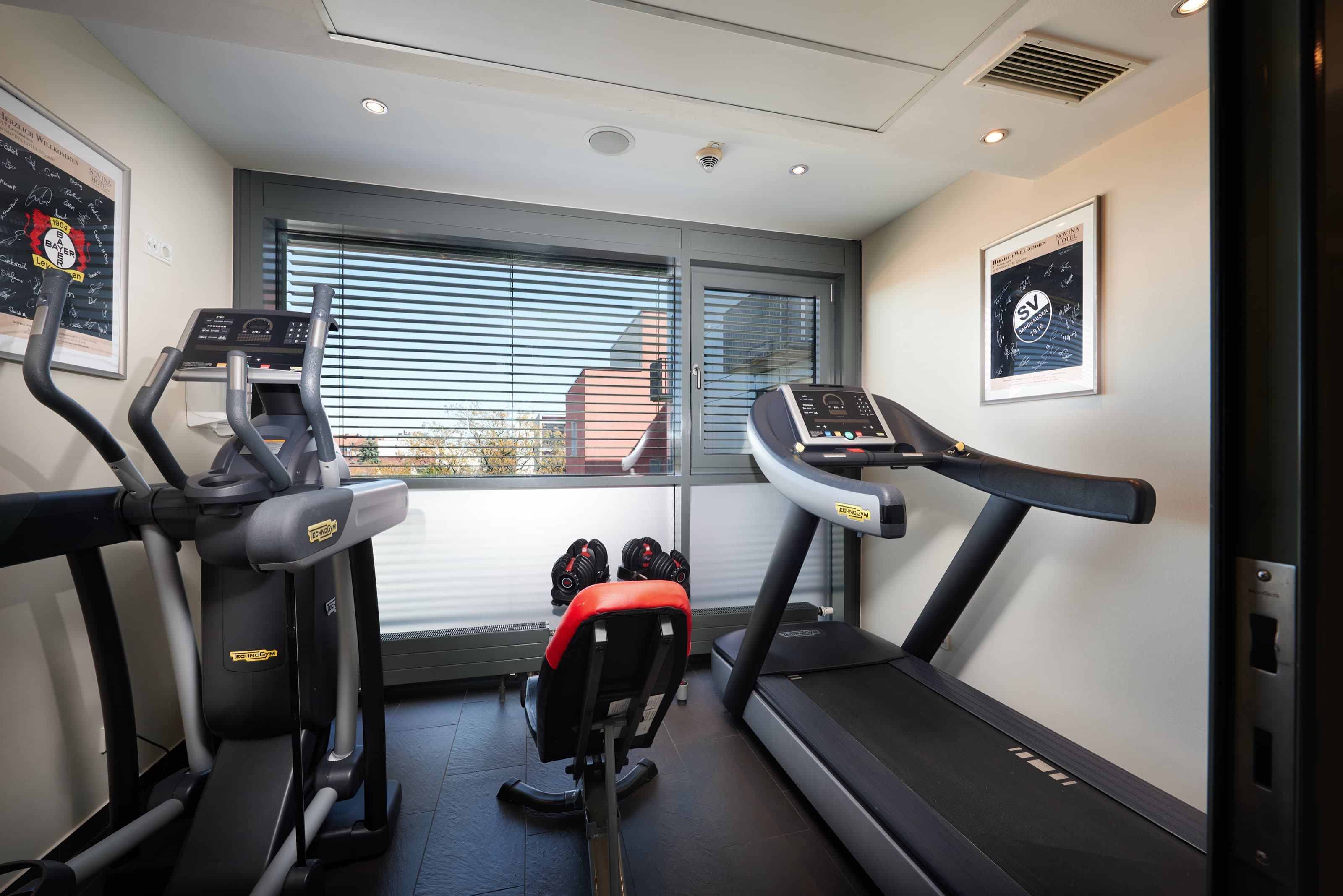 Fitnessraum im NOVINA Hotel Tillypark mit Laufbändern und Trainingsgeräten vor bodentiefen Fenstern